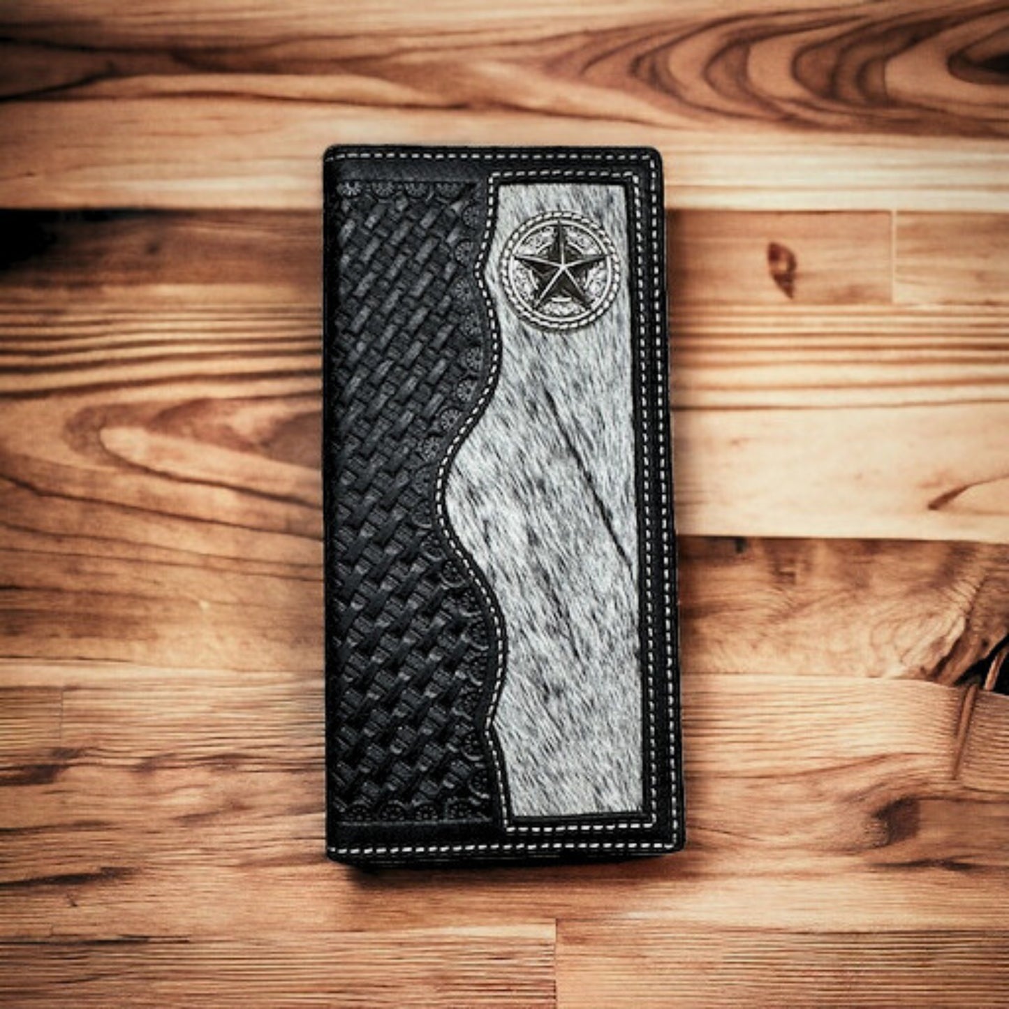 A stylish Lone Star Long Wallet Black W Cowhair Basketweave by Western Stakes with a textured black section and a gray fur-like panel on a wooden surface. This checkbook style wallet features white stitching along the edges and a star emblem in the top-right corner of the fur panel, making it an ideal cowboy accessory.