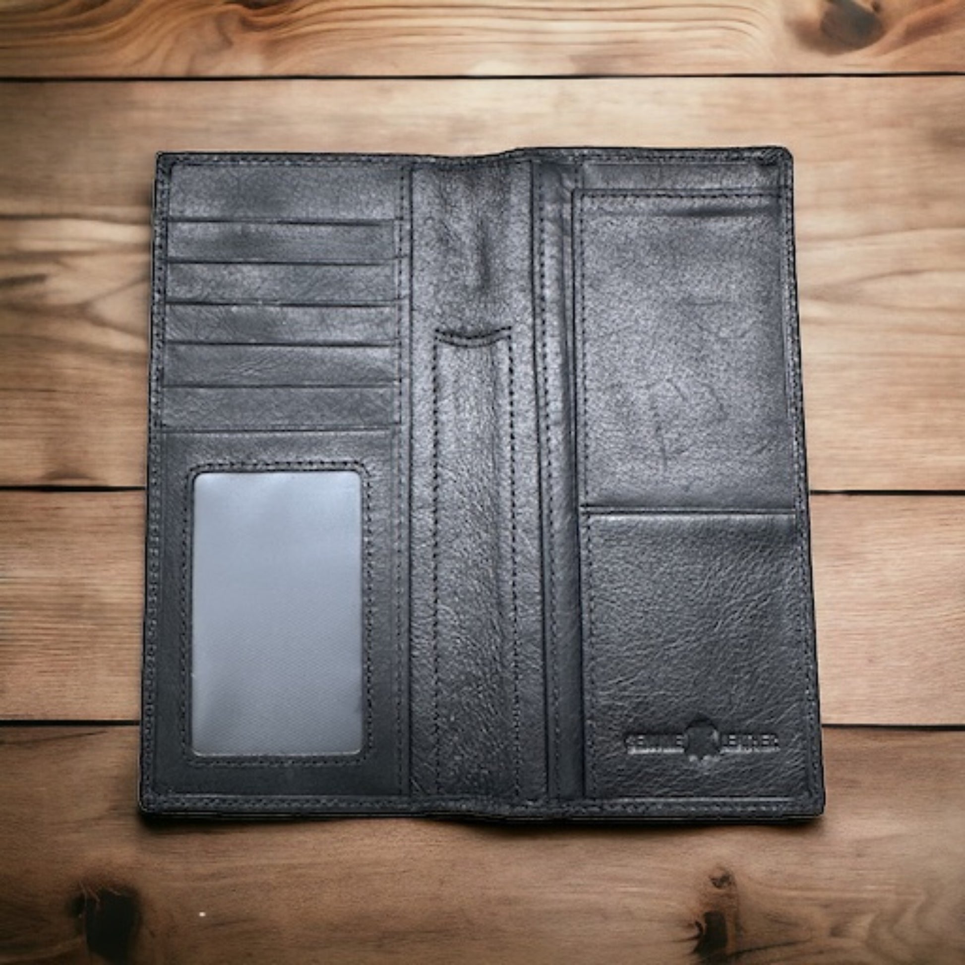 An open, black leather wallet displayed on a wooden surface exudes the charm of a Lone Star Long Wallet Black W Cowhair Basketweave by Western Stakes. It features multiple card slots, a transparent ID slot, a pocket for bills, and an embossed logo at the bottom right corner. The wood grain of the background adds texture to this elegant cowboy accessory.