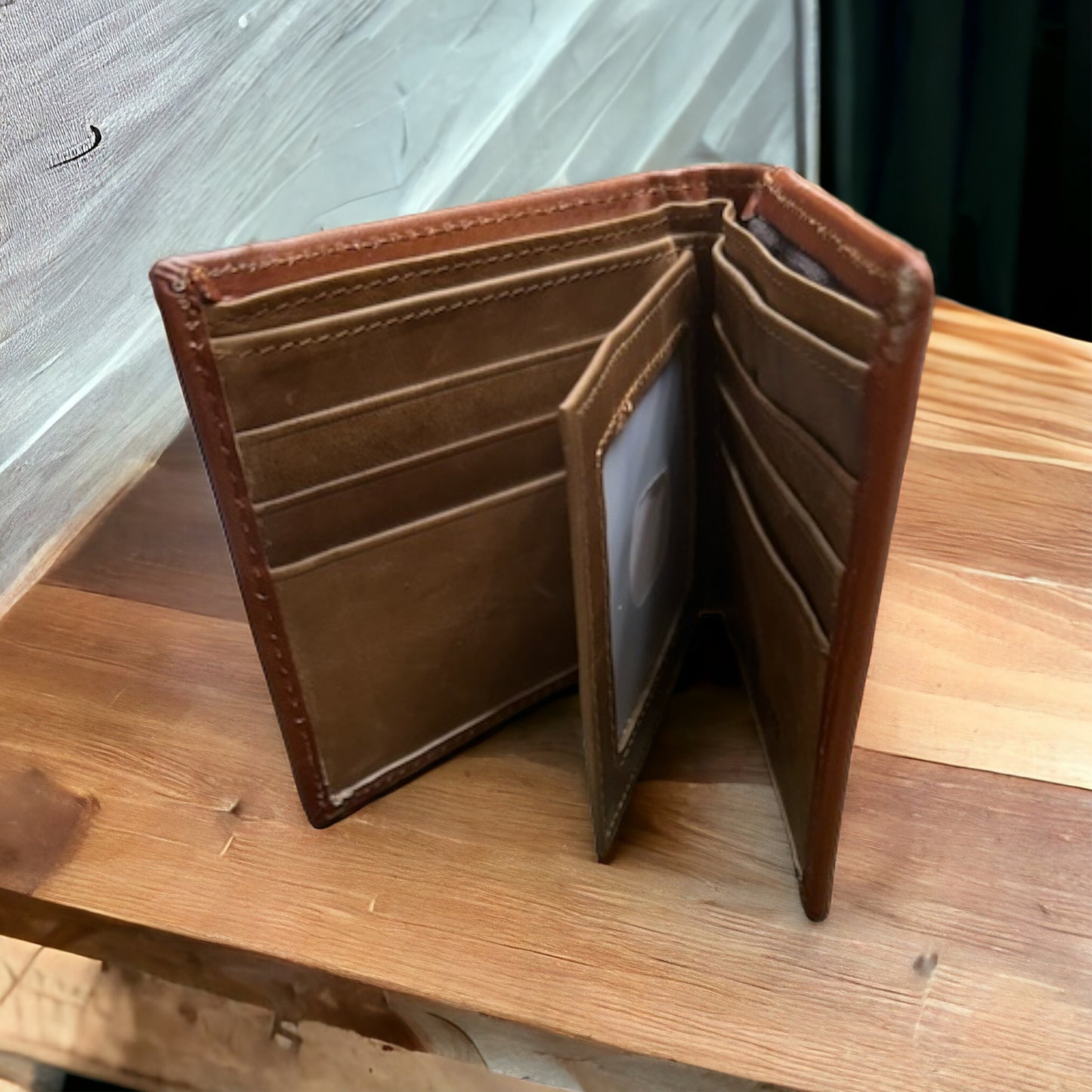 A Floral Leather Cowboy Wallet Brown & Teal by Western Stakes is open on a wooden surface, revealing multiple card slots, a clear ID window, and several pockets for cash and other items. This handcrafted cowboy wallet features an intricate floral cutout design on the front, making it a perfect addition to your collection of rodeo gifts.