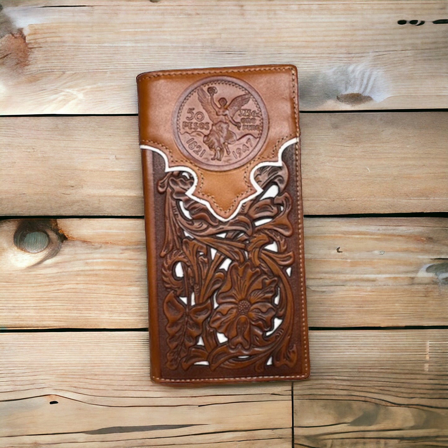 A Western Stakes Floral Long Wallet Brown White 50 Pesos with intricate floral cutout designs and a prominent, embossed Mexican 50 Peso coin motif from 1947 on the front. The brown leather wallet is placed on a wooden surface, showcasing its craftsmanship and design details.