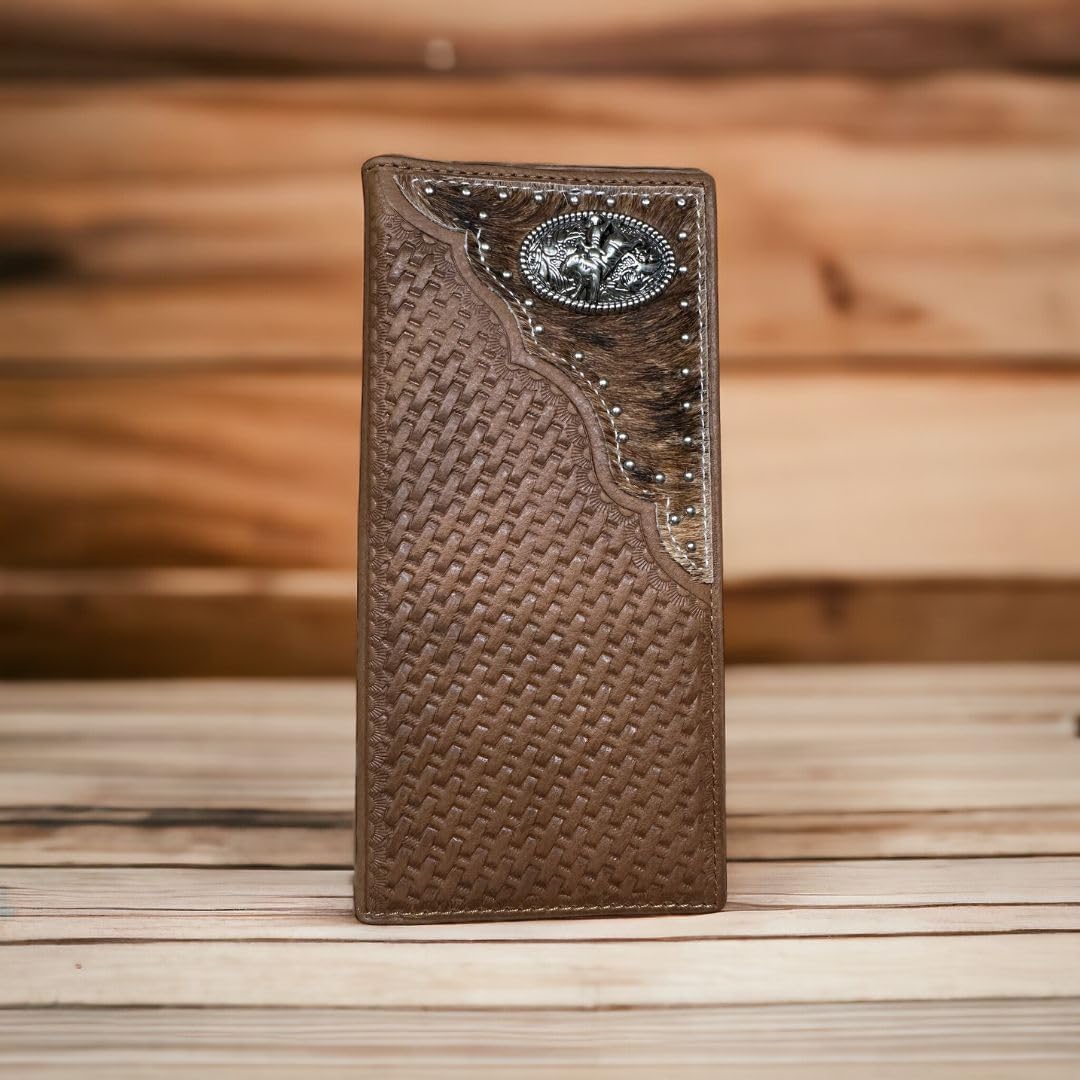 A Bull Rider Long Wallet W Cowhair Basketweave from Western Stakes is shown standing upright on a wooden surface. The wallet features a decorative metal emblem with a carved design and small silver studs lining the top edge. A patterned, darker leather strip accents the upper right corner, giving it a rugged charm.