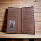 A brown genuine leather wallet, featuring a hand-tooled longhorn design, is open, displaying multiple card slots and a transparent ID window on the left side. Set against a wooden background, the text "Genuine Leather" is embossed on the bottom right corner of this Western Stakes Longhorn Long Wallet Brown Basketweave W/ Cow Hair.