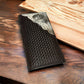 A Western Stakes Bull Rider Long Wallet W Cowhair Basketweave featuring a detailed woven pattern and a contrasting carved design with decorative stitching. The wallet is placed on a wooden surface, emphasizing its artisanal quality and elegant design, reminiscent of a classic Bull Rider Long Wallet.