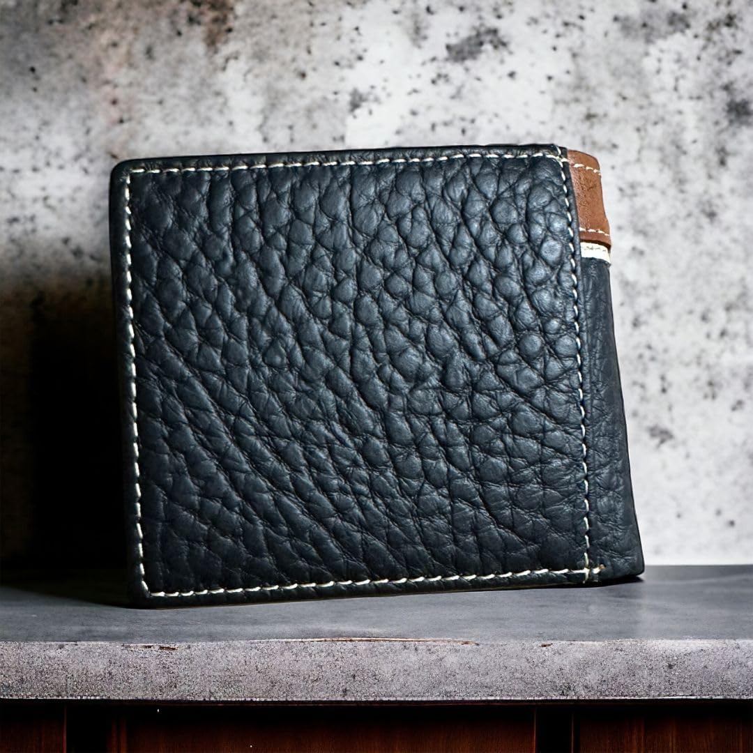 A black leather wallet with white stitching is standing upright against a textured gray background. The wallet, exuding Western flair, is closed, showing a pebbled texture. There is a small visible brown leather section on the right side adorned with a Texas Star Concho. The Mens Leather Wallet Texas Star Concho Black by Western Stakes perfectly captures the essence of rugged elegance.