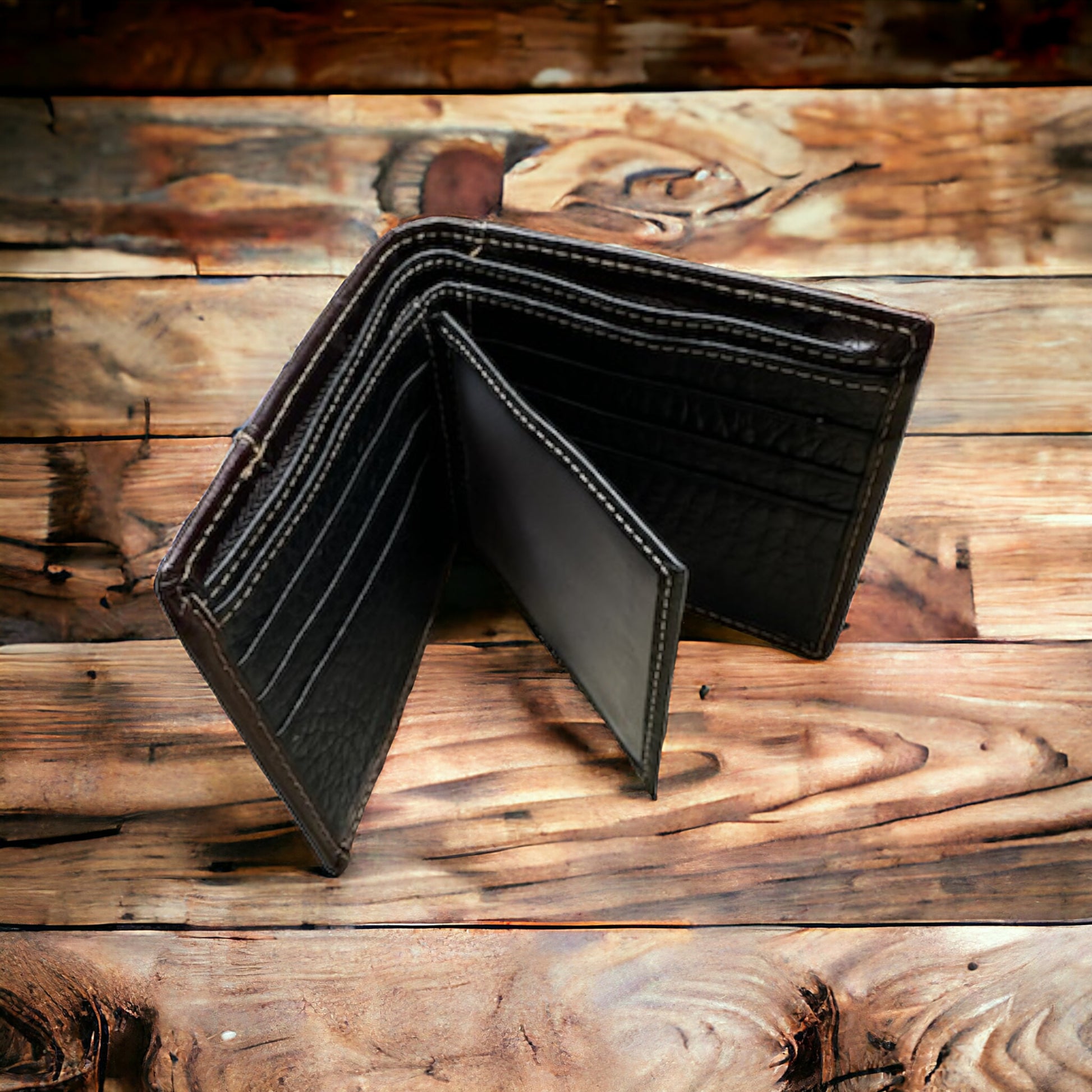 A black leather bifold wallet with multiple card slots and compartments is open and placed on a rustic wooden surface. The Floral Leather Cowboy Wallet Coffee Brown 50 Pesos by Western Stakes appears to be new and is neatly arranged.