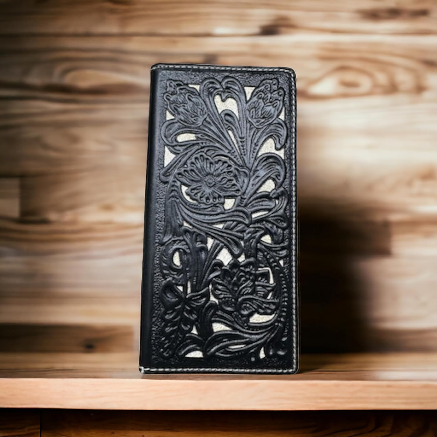 A Western Stakes Floral Long Wallet Black White with intricate floral cutout designs stands upright against a wooden background. The detailed pattern includes various flowers and leaves, creating an elegant and sophisticated look, perfect for those who appreciate a stylish checkbook-style long wallet.