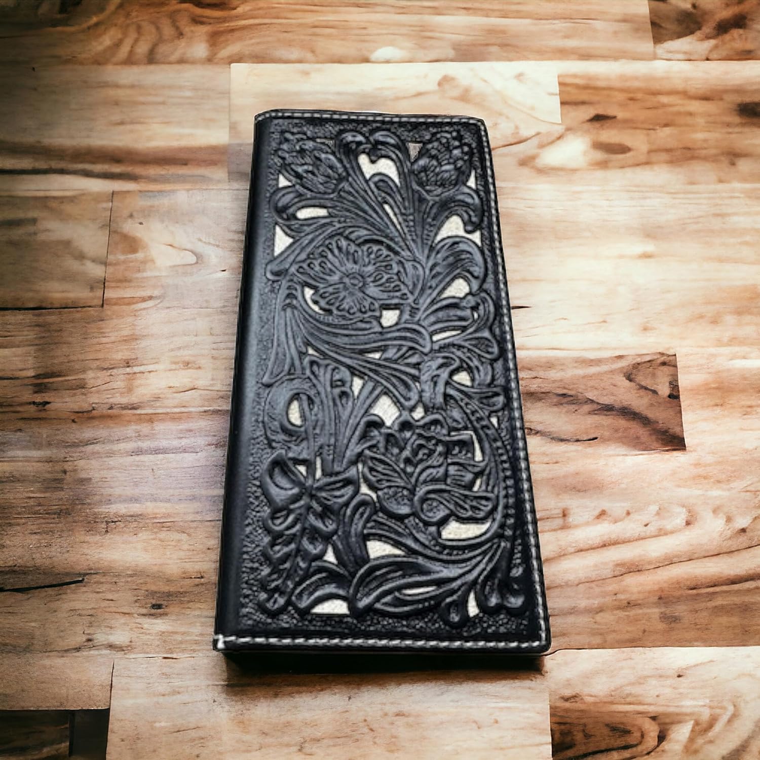 A Floral Long Wallet Black White from Western Stakes with an intricate floral cutout design is placed on a wooden surface. The design features various flowers and leaves, standing out prominently against the leather background.