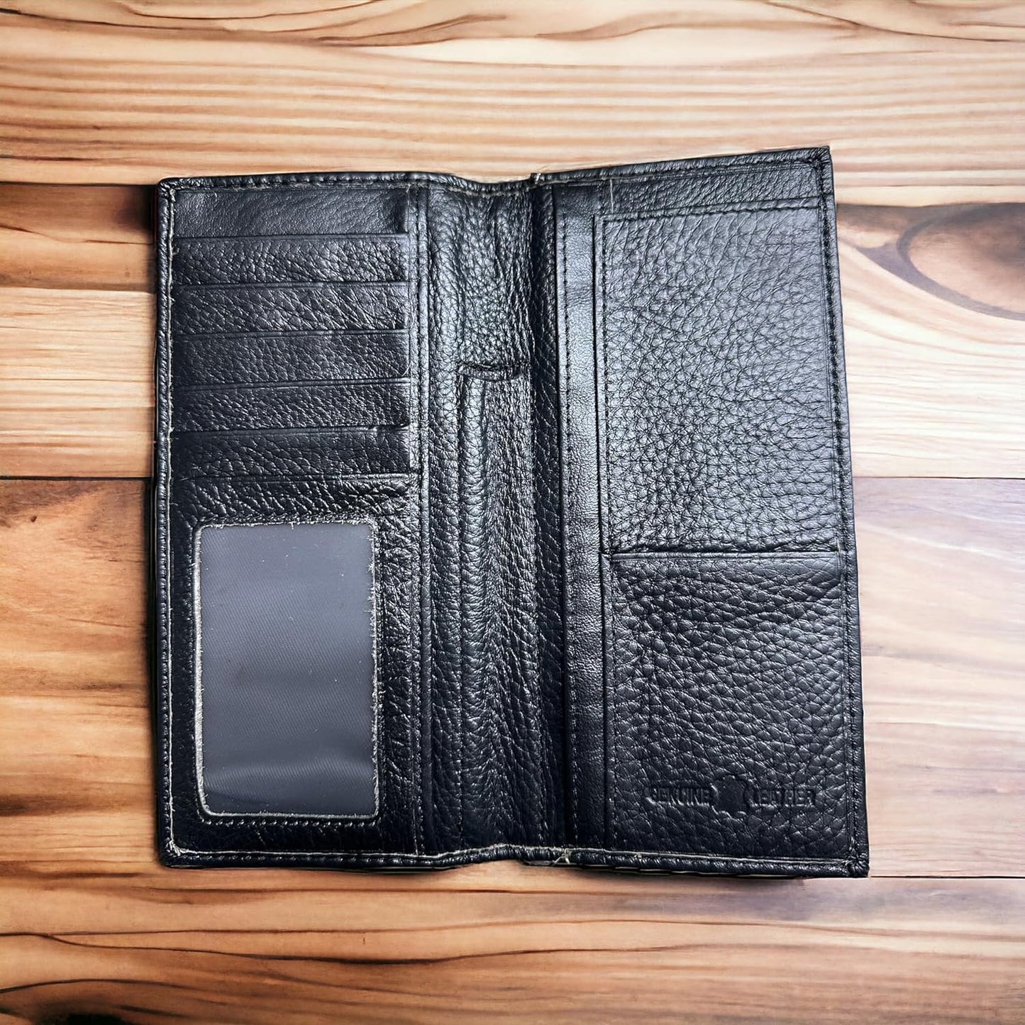 A fashionable Western Stakes Rodeo Long Wallet Black With Cowhair & Bull Rider Concho sits open on a wooden surface. The black leather wallet features multiple card slots, a clear ID window, and a currency pocket. The texture of the leather appears to be pebbled.