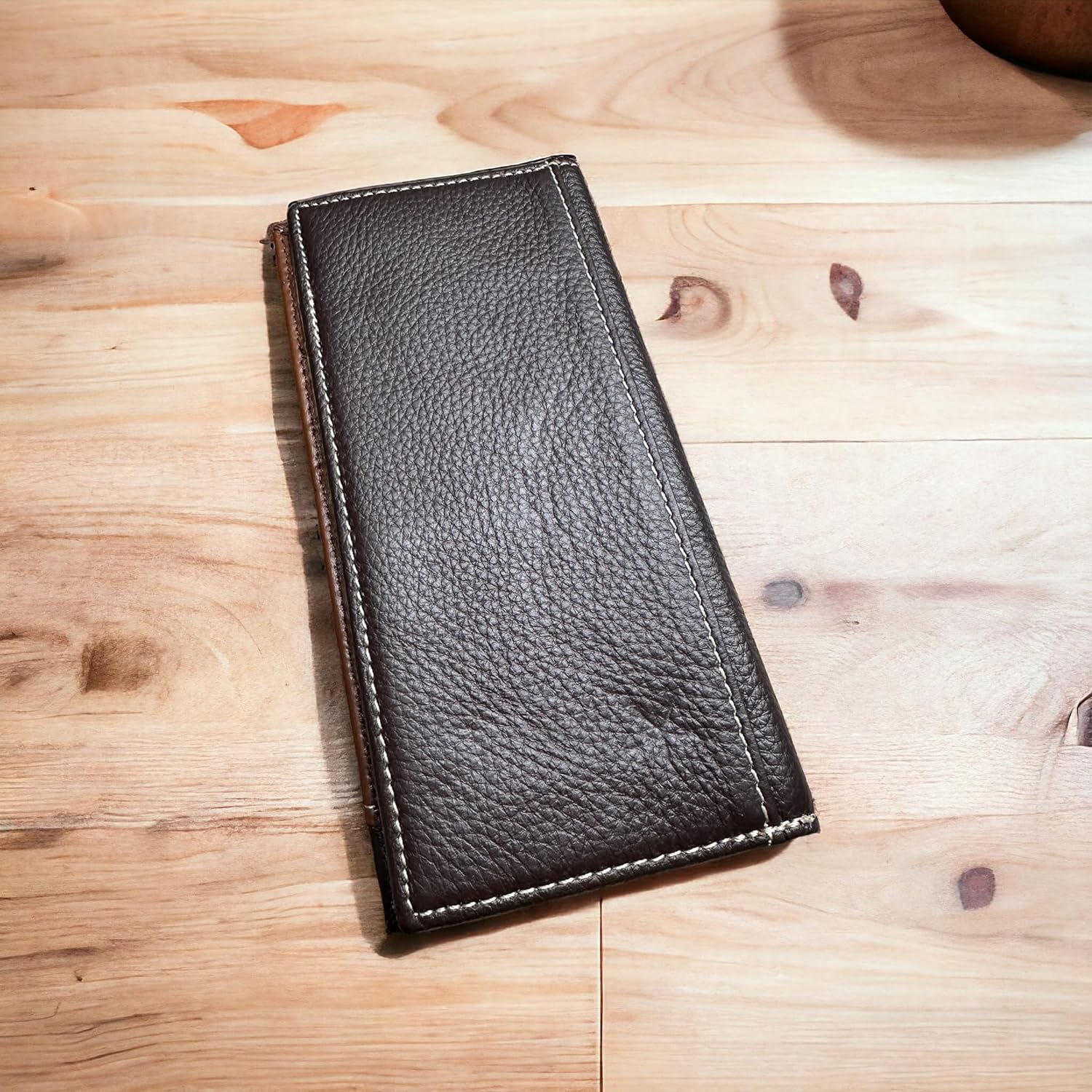 A dark brown leather wallet with a grainy texture lies closed on a wooden surface. The Floral Long Wallet Coffee Star Concho by Western Stakes features white stitching along the edges and is positioned horizontally in the center of the image—an ideal gift for him.