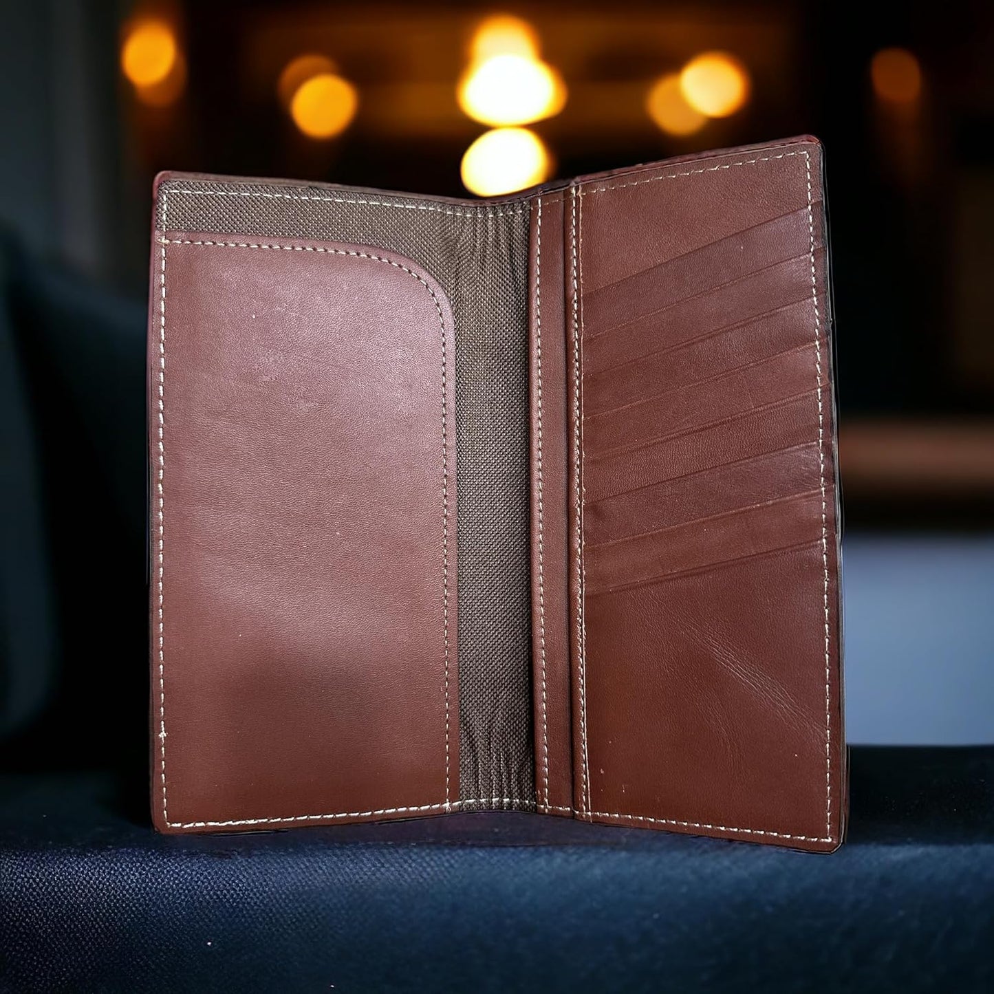 A Longhorn Long Wallet Brown With Cowhair & Concho is open, revealing multiple card slots on the right panel and an open pocket with a textured lining on the left panel. This Western Stakes wallet, a true western accessory, rests against a softly lit background with warm, blurry lights.